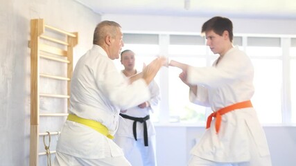 Wall Mural - Elderly man and young guy karatekas train karate fight in studio