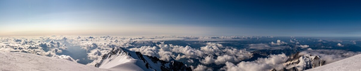 Panorama view Alpine tops from Mont Blanc glacier at morning, low clouds and clear blue sky