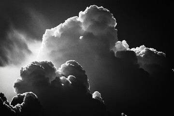 Dramatic black and white photo of fluffy clouds lit by the sun, casting a soft glow across the sky.