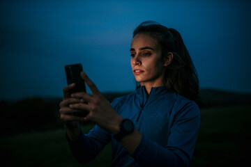 Happy young sportswoman smiling while holding a smartphone outdoors. Athletic young woman taking a break from working out.