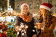 © Lomb - Joyful friends celebrating Christmas with sparklers and drinks at festive market, holiday cheer and togetherness