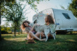 © Halfpoint - Young couple is on a camping trip in nature playing with dog, sitting in front of caravan. Caravan traveling for young people.