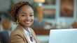© visoot - African corporate professional female internal audit manager in office seated in office chair working, happy and smiling, formal professional hairstyle and formal attire, laptop on table.