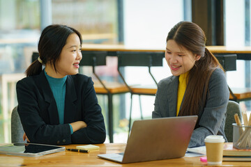 Two young Asian businesswomen discussed investment project work and planning strategy. Business people talk together on laptop computers at the office.