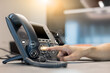 © chinnarach - close up employee call center man hand point and press button number telephone voip machine in the office desk with virtual icon of communication technology for business and contact us concept