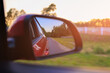 © Kozlik_mozlik - The sun is reflected in the mirror, evening road. View in the side rear view mirror of a red car driving along the highway