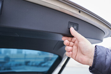 Close-up of male hand opening a car trunk with emergency button.