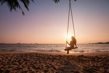 Wall Mural - silhouette of woman on rope swing on tropical sea beach, dream vacation travel, sunset landscape