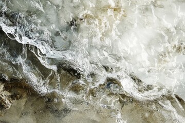 A detailed close-up of textured ice meeting sand at the water's edge, capturing an intriguing natural interface with dynamic lines and organic patterns.