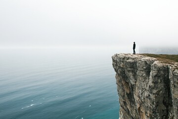 A lone figure stands on a cliff with a misty sea horizon, encapsulating solitude and adventure under the dramatic sky typical of modern landscape photography.