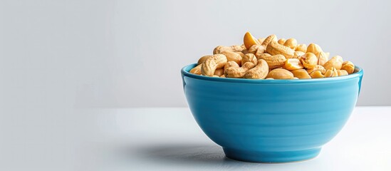 Blue bowl with roasted peanuts on white backdrop with copy space image