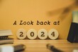 © Debalina - A Look back at the year 2024 concept with wooden chips and inscription. Best events of the year, highlights, recap, performance, evaluation of 2024. Office desk background.