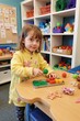 © Aira - Smiling Toddler Engaging in Sensory Play with Colorful Toys in a Bright Classroom