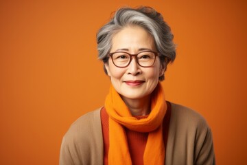 Wall Mural - smiling senior asian woman in scarf and glasses on orange background