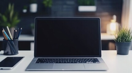 close-up of a laptop open on a white surface. A tablet PC, a smartphone, pencil holders, and paper graphics are all close by. Houseplants and a shadowy wall are in the backdrop. Workplace empty.