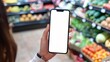 © Natasha  - Hand holding smartphone with blank screen in grocery store produce aisle..Mock up. Copy space