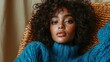 © Maximages  - A woman with soft curls rests comfortably indoors, enveloped in a plush blue sweater, her expression serene as she embodies warmth and relaxation in a cozy setting.
