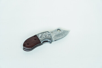 Mini folding knife with patterns on some parts of the blade isolated on a white background. Close-up view of a mini folding knife used for various outdoor or survival activities