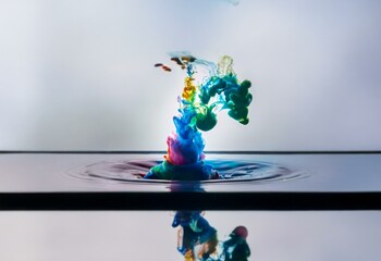 Fototapete - Colorful ink swirls and spreads in a dark blue liquid against a light grey backdrop.