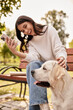 © LIGHTFIELD STUDIOS - A joyful woman in cozy autumn attire smiles at her dog while relaxing in the park.