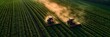 © Prasong Takham - Two red tractors plowing and cultivating rows of green agricultural fields in a scenic rural landscape. Aerial overhead view of modern farming equipment working in open countryside.