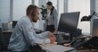 © Framestock - In modern office: Male financial trader or stockbroker in headset works on computer, communicates with business client on call, monitors stock market, makes notes. Female colleague in the background.