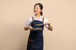 © PBXStudio - Beautiful Asian female coffee shop owner wearing apron. She holds a frying pan and wooden spatula with copy space.