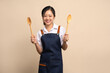 © PBXStudio - Portrait of young Asian woman in apron on beige background. Cooking and entrepreneurship concept.