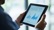 © Oulaphone - A person analyzing data on a tablet, showcasing a visual graph with fluctuating statistics in a modern workspace.