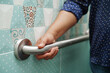 © manassanant - Asian woman use toilet support rail in bathroom, handrail safety grab bar, security in nursing hospital.