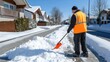 © lililia - The worker shovels snow from the sidewalks, ensuring safe passage near parked vehicles during a snowy day