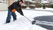 © lililia - A young man is joyfully shoveling snow outside his home, surrounded by a picturesque winter landscape and covered houses.
