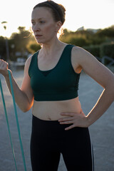 Wall Mural - Woman doing sports exercises with resistance band at sunset