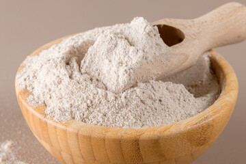 Buckwheat flour in a wooden bowl and raw buckwheat grain on beige monochrome background, close up. Alternative flour, gluten free flour, healthy nutrition