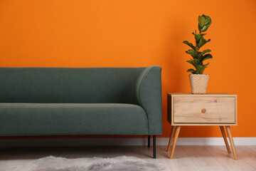 Canvas Print - Stylish sofa and side table with green houseplant near orange wall indoors