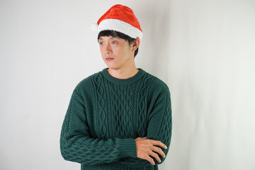 Young asian man wearing santa clause hat and green long sleeved sweater is showing no expression face, isolated over white background. Concept for Christmas Holiday and New Year Party