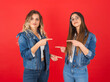 © Designerant - Pointing at each other, portrait of young caucasian two female friends happy fun confident smiling women pointing each other. Posing together wear denim jackets talking speaking over red background.