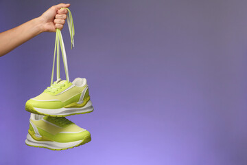 Wall Mural - Woman holding pair of stylish sneakers against color background, closeup. Space for text