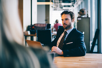 Back view of intelligent male director sitting at table with modern laptop computer and communicating with female colleague about financial strategy for corporate company, concept of entrepreneurship