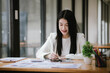 © Witoon - A happy Asian female businessman is at a modern desk. Financial reports and online documents using laptops She analyzed the organization's strategy and cooperated with her team for success.