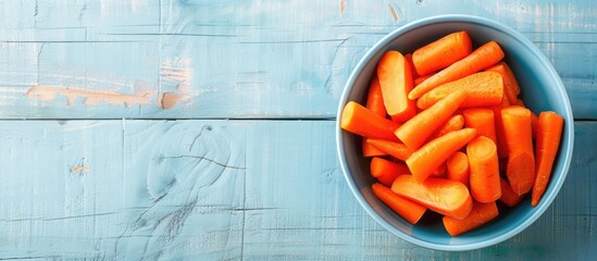 Carrot pieces arranged in a bowl on a pale blue wooden surface with a blank area for adding text in a copy space image