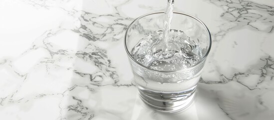 Wall Mural - Water being poured into a glass on a white marble table with copy space image