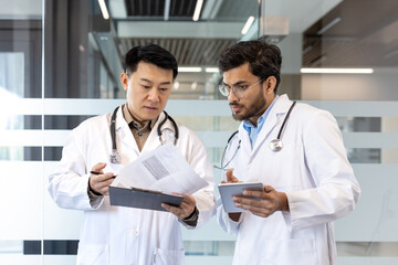 Doctors collaborating in modern office reviewing medical documents on clipboard and tablet. Focus on teamwork, healthcare, technology. Professional setting with insightful discussion.