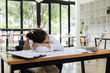 © wichayada - Exhausted Office Worker Sleeping at Desk with Laptop and Documents in Modern Workspace