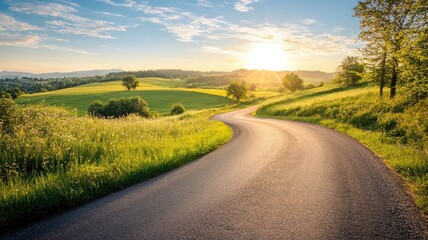 Wall Mural - Serene country road curving through green fields at sunset with distant forest and radiant sky