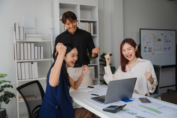 Triumphant Team Meeting: Celebrating Success. Three young Asian business professionals express unrestrained joy at a modern office, gathered around a laptop displaying positive results.