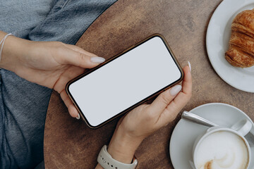 Mockup woman's hand holding using smart phone with white blank screen at coffee shop, mobile app design and advertising, online marketing