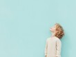 © Yuliya - A small child isolated on a light blue background. A red-haired boy in white clothes against a blue wall looks sideways and upward. Child in profile looking up, copy space.
