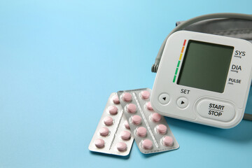 Poster - Blood pressure measuring device and pills on light blue background, closeup. Space for text