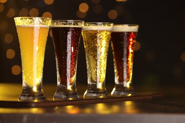 Canvas Print - Glasses with different types of beer on wooden table against blurred lights, closeup